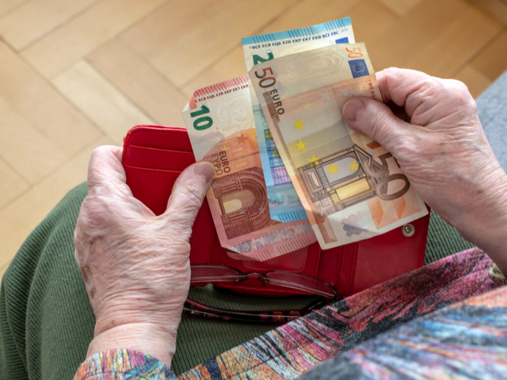 Elderly hands putting cash into a wallet